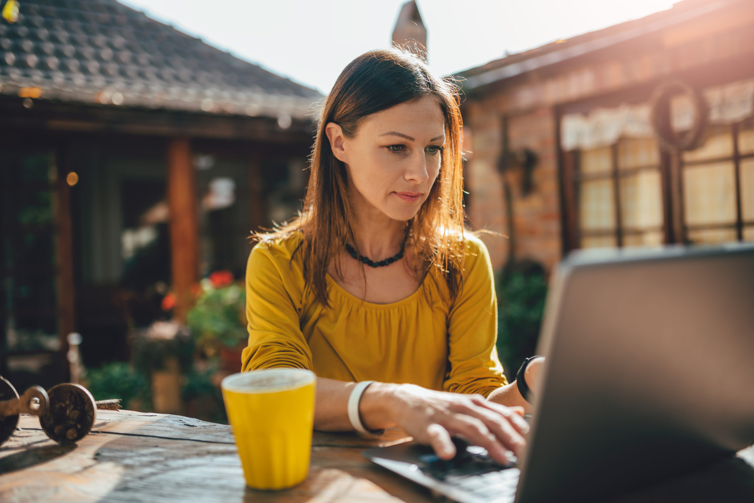 Women wearing yellow shirt using laptop at backyard patio